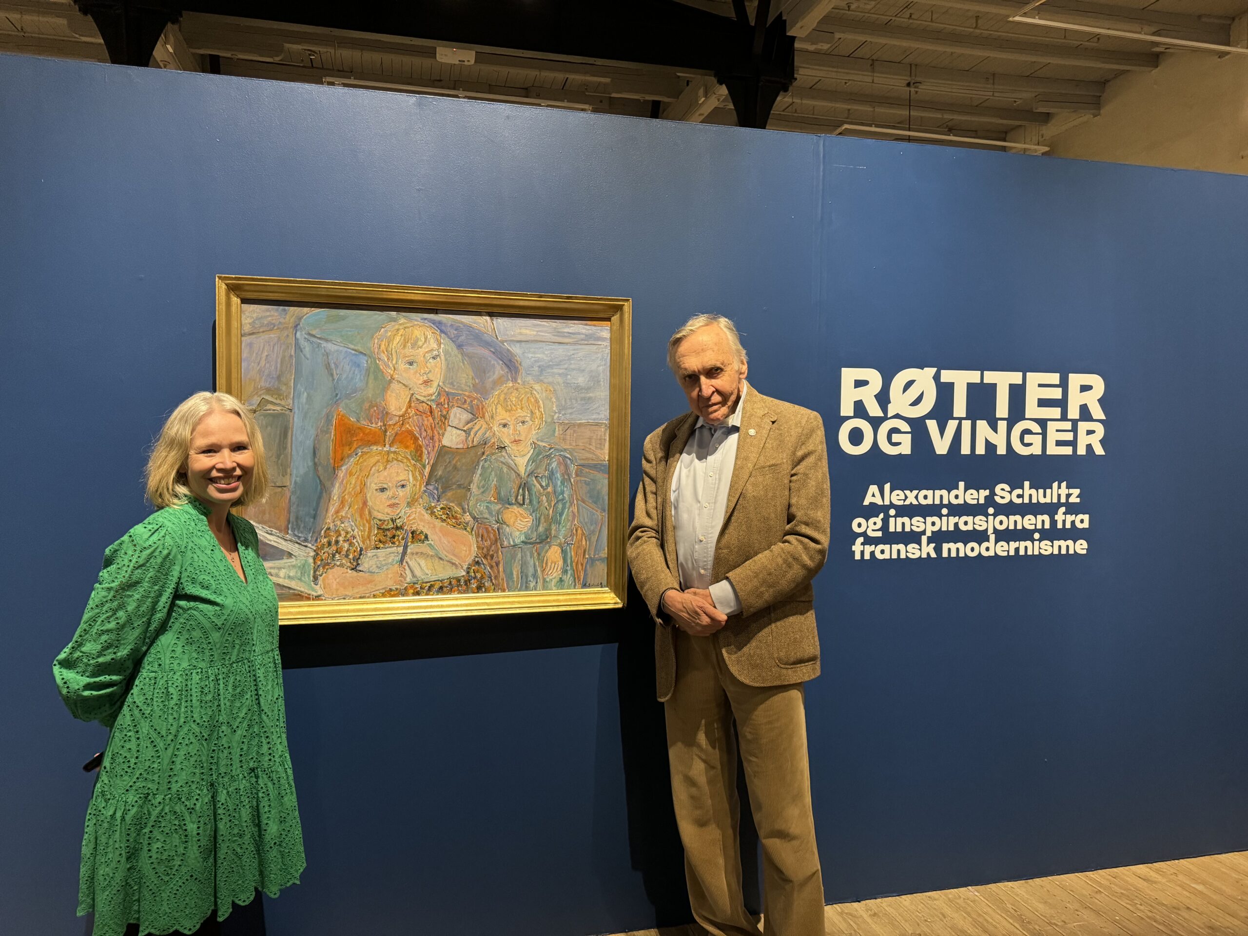 Forsker Målfrid Vangen og sønn av kunstner Schultz står foran kalt bilde på utstillingsvegg.